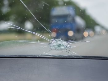 The Broken Windshield Of The Car From Flying Stone. The Hole In The Glass, Chips And Debris, Cracks In Strips. The Glass Reflects The Sky With Clouds.